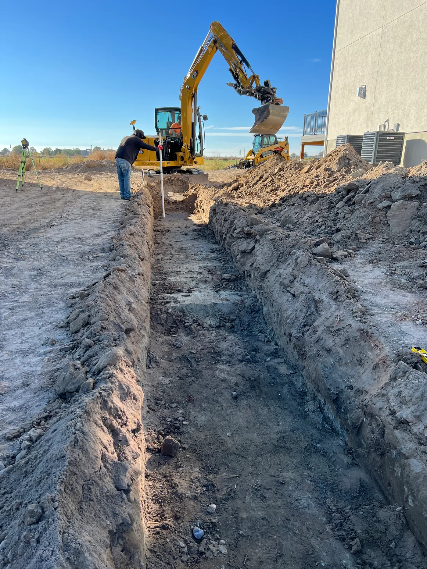 A crew member checking grade in a footing trench beside a new building