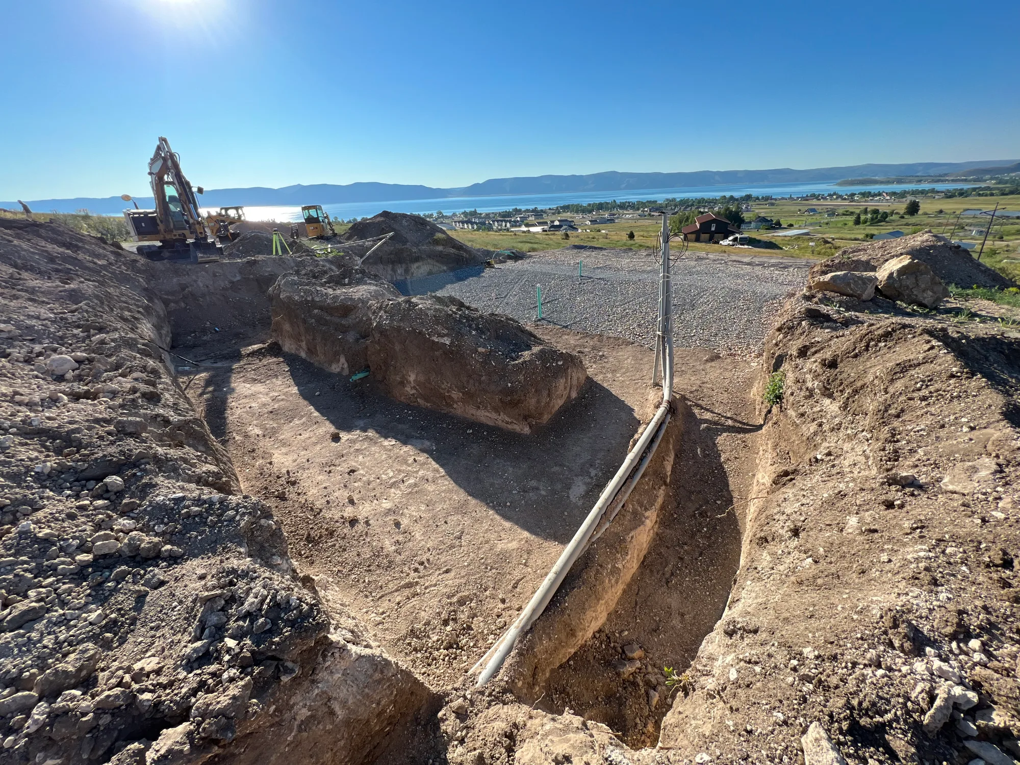 A hillside excavation with a utility conduit along the trench wall and a lake beyond