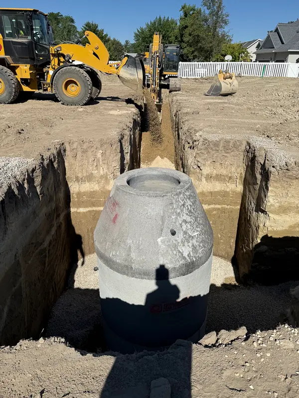A concrete manhole cone set in a sewer trench, marked up with an arrow