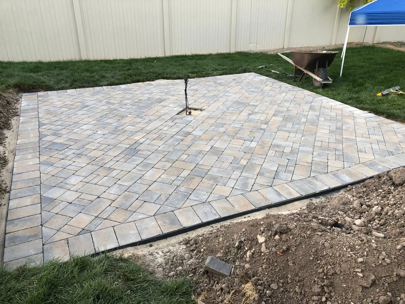 Pavers laid in a herringbone pattern on new sod, with a capped gas line standing up in the middle where the fire pit will go