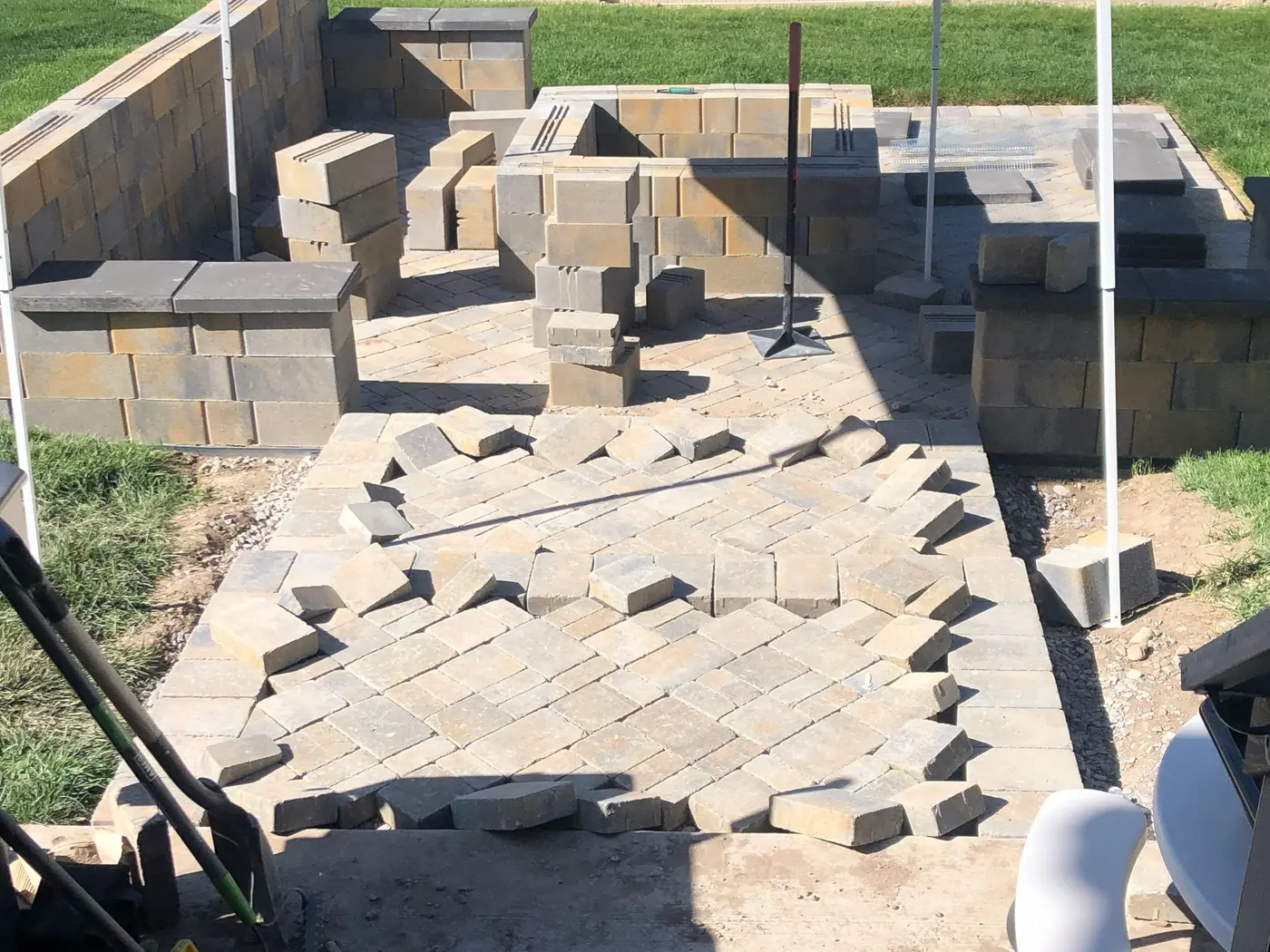 Looking down from the deck at the patio: a square block fire pit and seat walls going up, block and caps stacked around