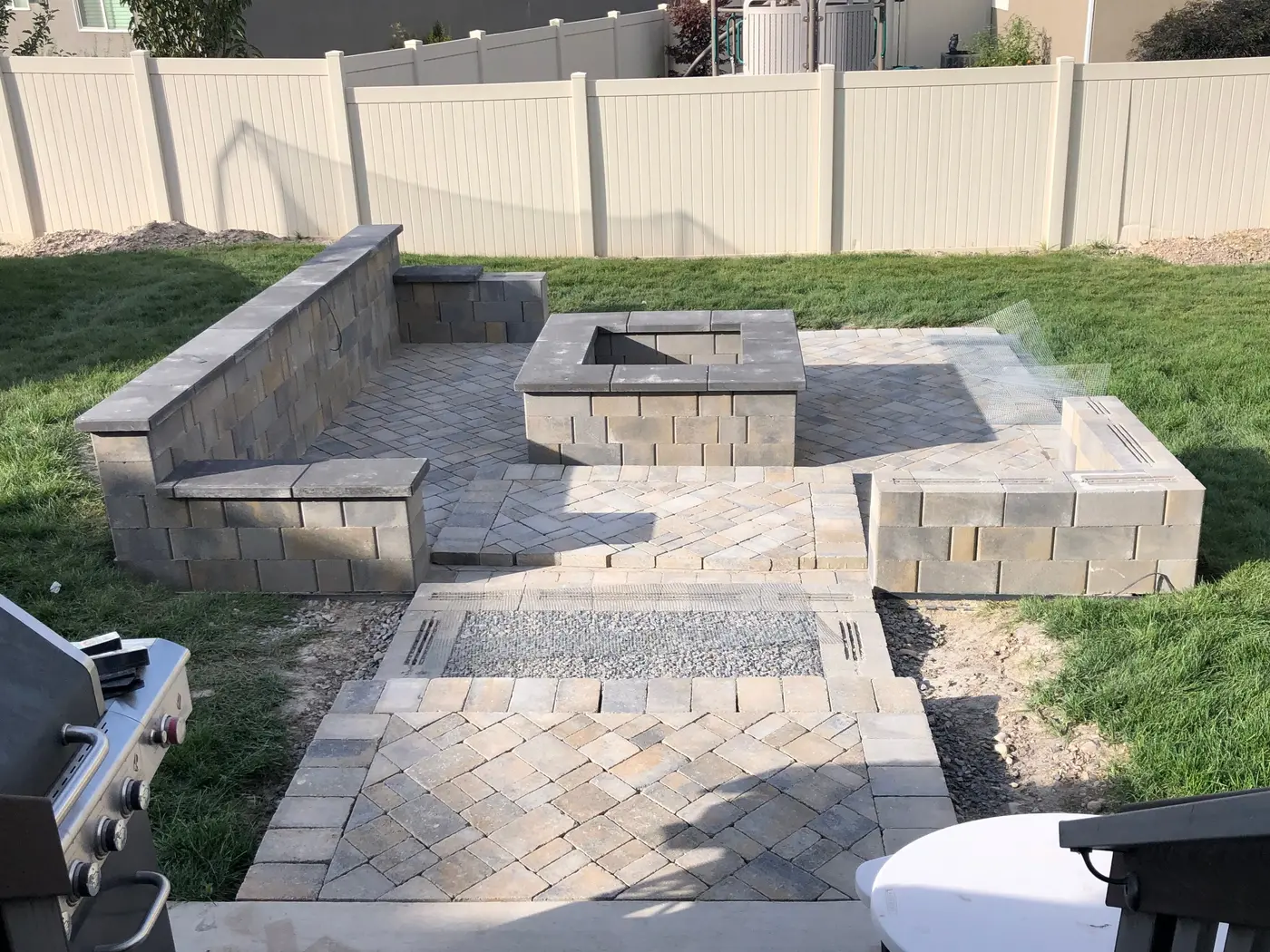 The paver patio with a capped square fire pit, L-shaped seat walls and paver steps down from the deck