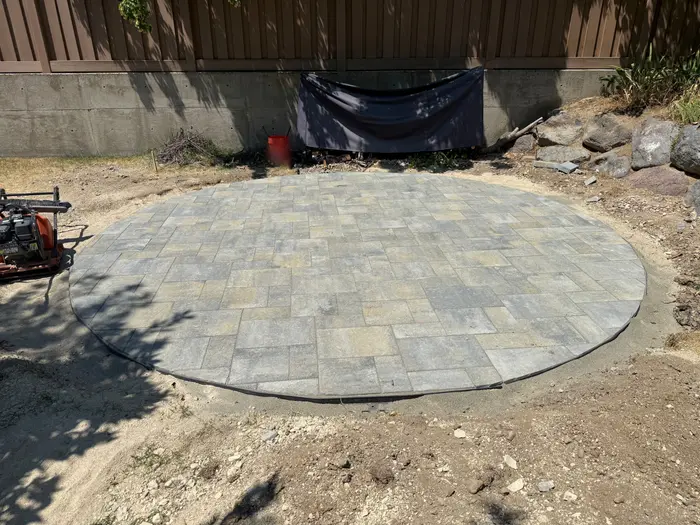 A new round paver patio on a compacted base beside a concrete retaining wall