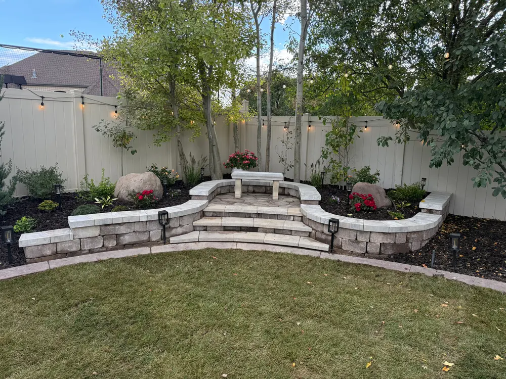 Curved block seat walls and paver steps up to a flagstone patio, planting beds with lights and a new lawn