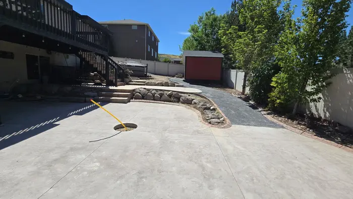 A new stamped concrete patio with a round fire pit ring set in it, a gravel path curving past a shed
