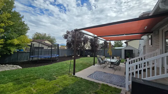 A finished backyard with new sod, bark-mulch beds with boulders along the fence and a patio under shade sails
