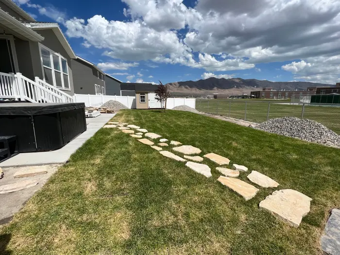 A flagstone stepping-stone path across new sod in a new-home backyard, mountains and big white clouds behind
