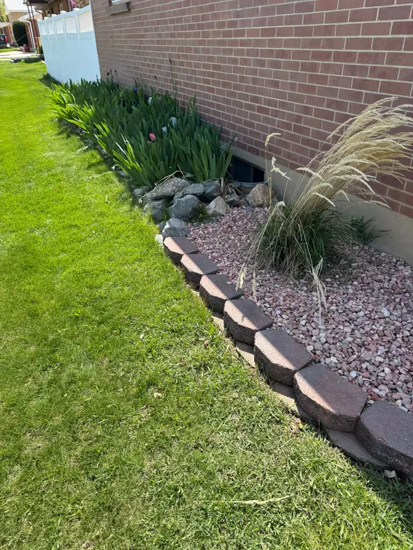A side-yard bed of red rock, ornamental grasses and iris along block edging next to a lawn