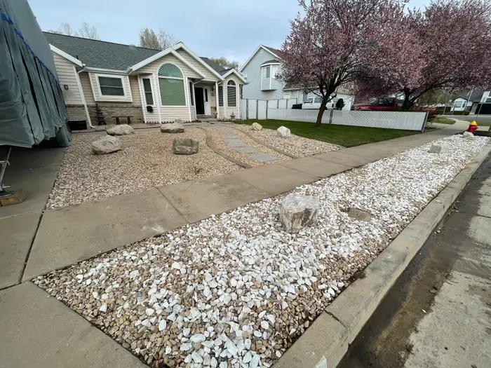 A finished xeriscape front yard: a white rock park strip, tan rock beds with boulders and a flagstone path between concrete curbing