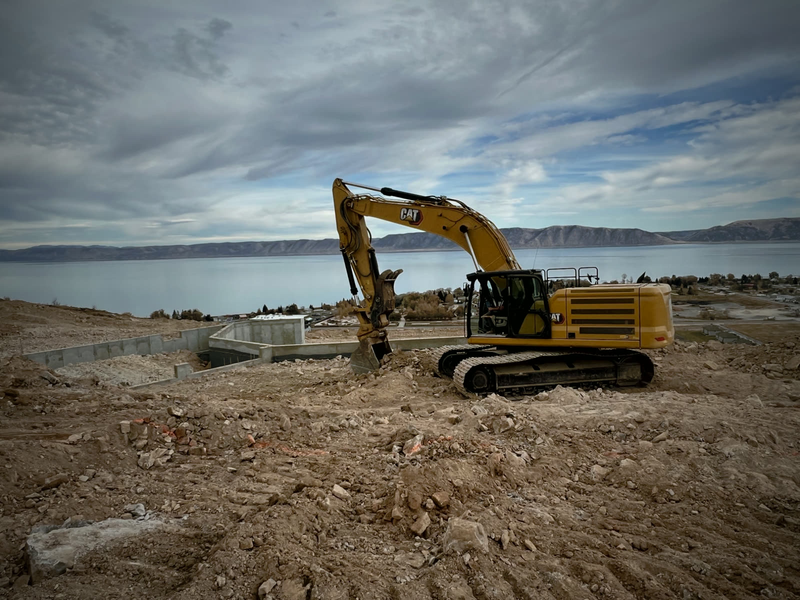 A Woodward Co. CAT excavator digging a hillside site above the lake
