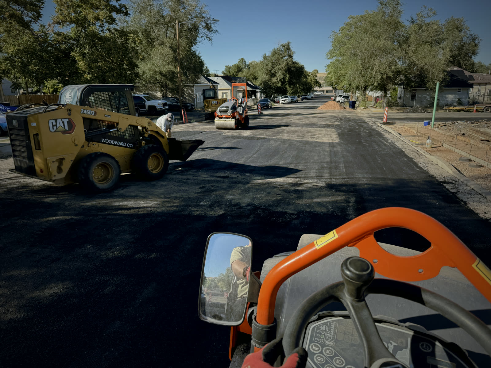 From the operator's seat of a roller: a Woodward Co. CAT skid steer spreading asphalt down the street